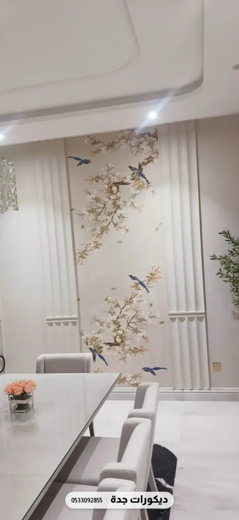 جدار بأغصان أزهار وطيور صغيرة خلف طاولة طعام بيضاء